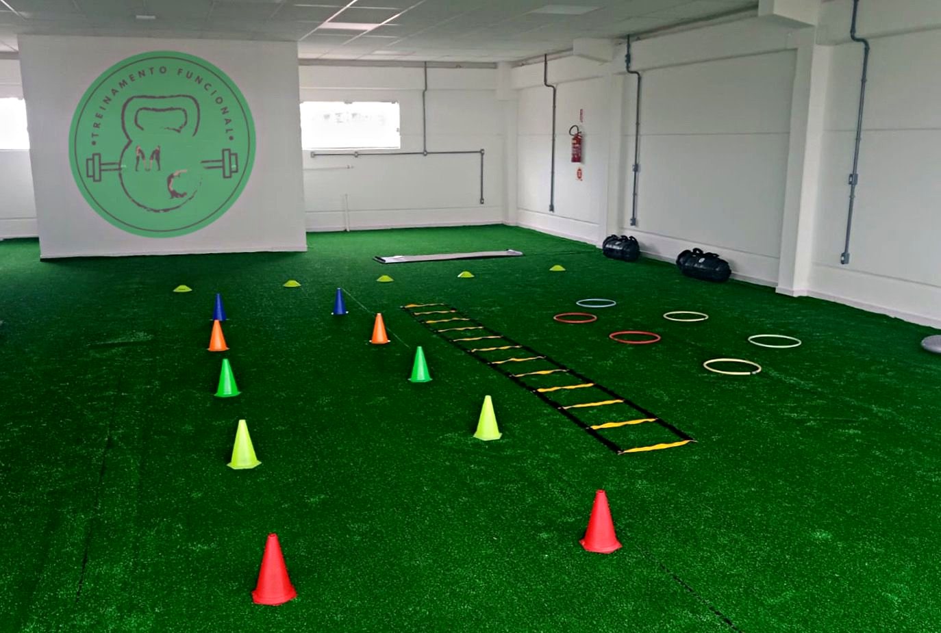 Sala de treinamento funcional da MC com grama sintética, cones e escada de agilidade